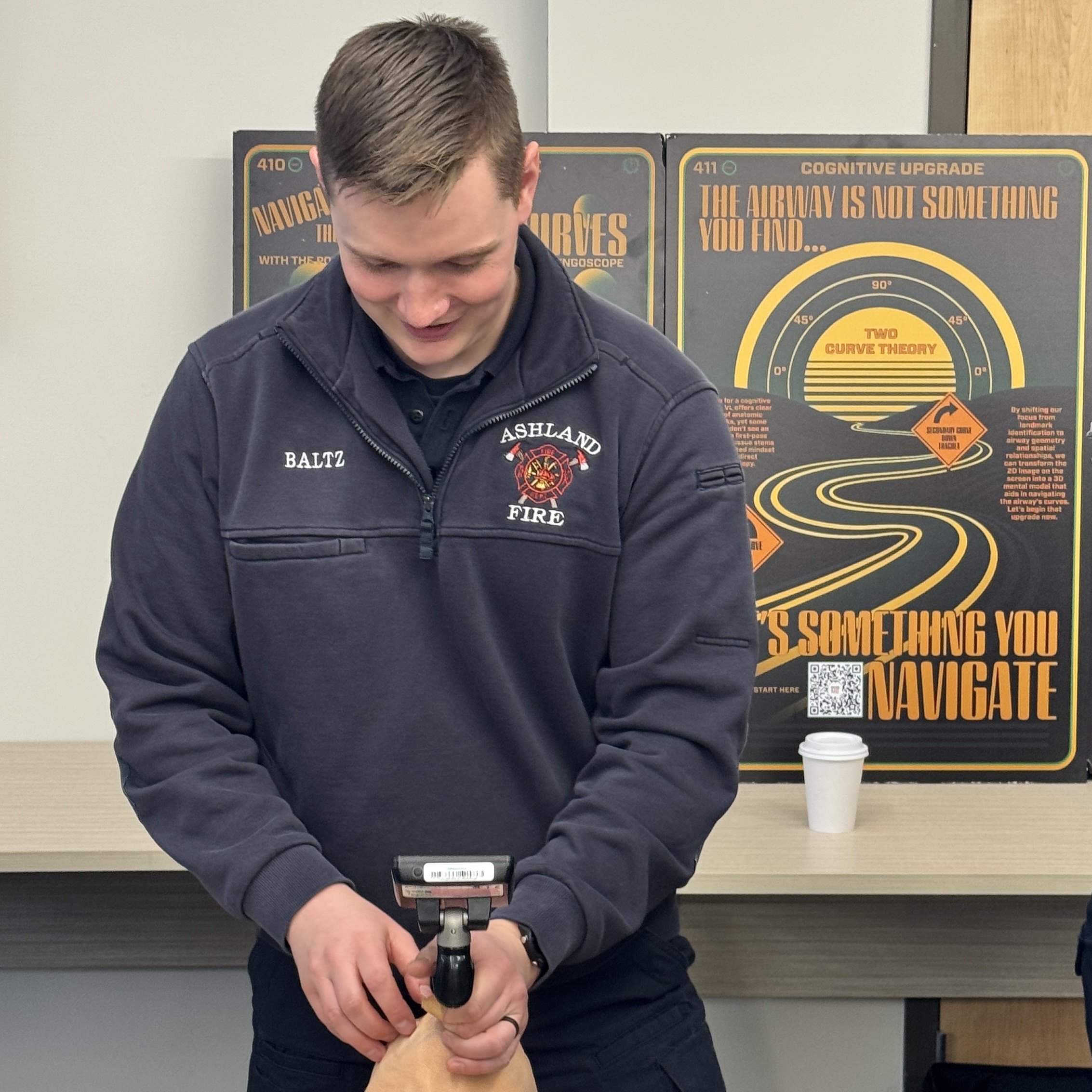 A learner rehearses airway instrumentation with two PACscape posters behind him.