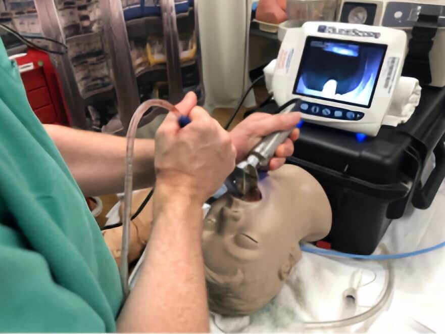 A healthcare professional performing airway management on a training mannequin using a video laryngoscope and suction catheter.
