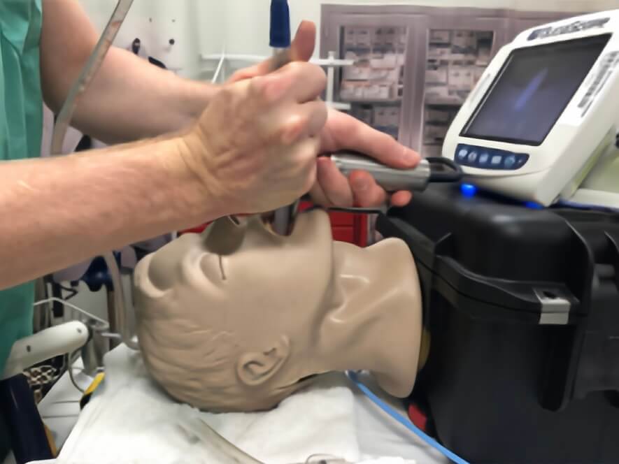 A healthcare professional demonstrating the SALAD technique on a training mannequin, using a laryngoscope and suction catheter, with medical equipment in the background.