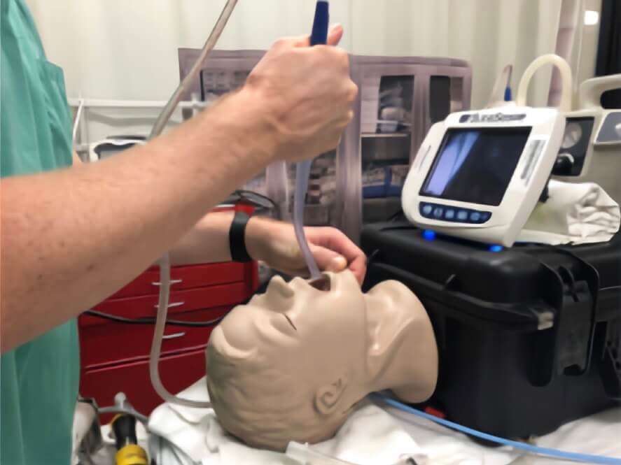 A healthcare professional demonstrating the SALAD technique on a training mannequin, using a suction catheter and laryngoscope in a clinical setting.