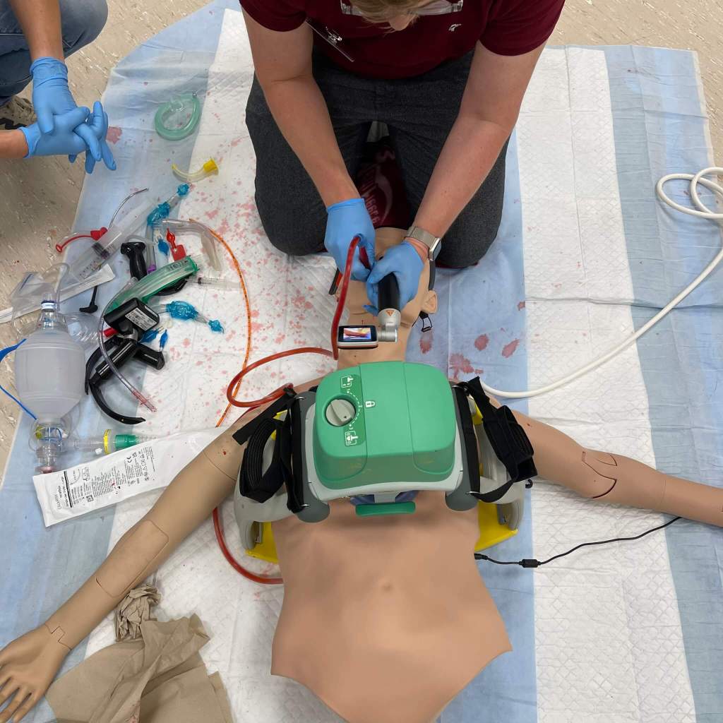 A healthcare professional performing airway management on a training mannequin, surrounded by various medical tools and equipment.