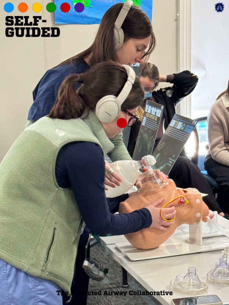 Two individuals wearing headphones are practicing airway management techniques on a medical training mannequin in a classroom setting.